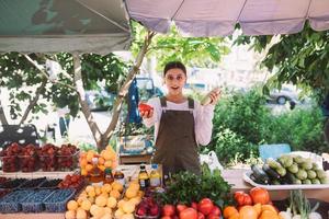 vendedora joven que sostiene el calabacín y el tomate en manos foto