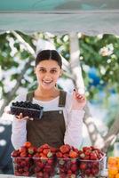Young positive saleswoman at work, holding currants in her hands photo