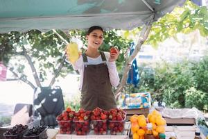 Young saleswoman holding bell pepper and tomato in hands photo