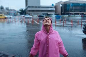 Young smiling woman in a pink raincoat enjoying a rainy day. photo