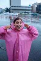 joven mujer sonriente con un impermeable rosa disfrutando de un día lluvioso. foto