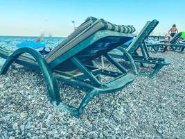 hot, tropical country with sea and mountains. pebbles on the beach, small stones near the water. there is a bed on the ground. tourists in bathing suits swim nearby photo