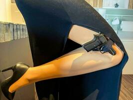 una mujer con un vestido negro de noche sostiene una pistola con medias. Pistola negra, pequeña y compacta. arma militar agente especial en una misión foto