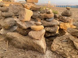 una pirámide de piedras apiladas una encima de la otra en la playa y arena con pequeñas piedras naturales multicolores en la orilla contra el fondo del mar al atardecer foto