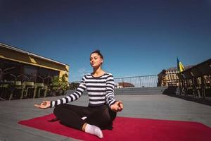 Young woman meditating in lotus pose at roof of the building photo