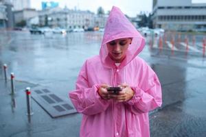 una mujer joven con un impermeable mirando el teléfono inteligente foto