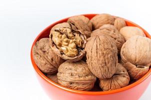 Montón de nueces en un recipiente naranja sobre un fondo blanco. foto