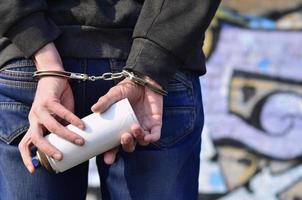 A rear view of an arrested street artist in handcuffs with aeros photo