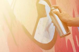 A hand with a spray can that draws a new graffiti on the wall. Photo of the process of drawing a graffiti on a wooden wall close-up. The concept of street art and illegal vandalism