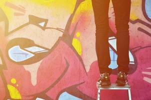 A young graffiti artist paints a new graffiti on the wall. Photo of the process of drawing a graffiti on a wall close-up. The concept of street art and illegal vandalism