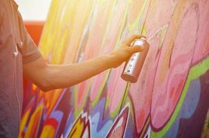 A young red-haired graffiti artist paints a new graffiti on the wall. Photo of the process of drawing a graffiti on a wall close-up. The concept of street art and illegal vandalism