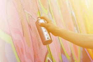 A young red-haired graffiti artist paints a new graffiti on the wall. Photo of the process of drawing a graffiti on a wall close-up. The concept of street art and illegal vandalism