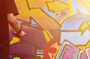 A hand with a spray can that draws a new graffiti on the wall. Photo of the process of drawing a graffiti on a wooden wall close-up. The concept of street art and illegal vandalism