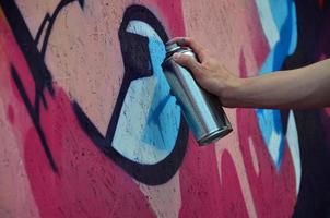 A hand with a spray can that draws a new graffiti on the wall. Photo of the process of drawing a graffiti on a wooden wall close-up. The concept of street art and illegal vandalism