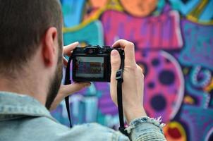 un joven grafitero fotografía su cuadro completo en la pared. el chico usa tecnología moderna para capturar un colorido dibujo de graffiti abstracto. centrarse en el dispositivo de fotografía foto