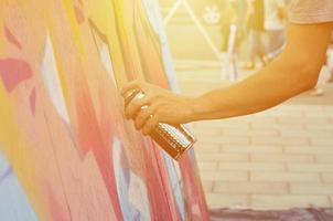 A hand with a spray can that draws a new graffiti on the wall. Photo of the process of drawing a graffiti on a wooden wall close-up. The concept of street art and illegal vandalism