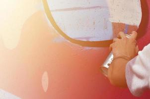 A hand with a spray can that draws a new graffiti on the wall. Photo of the process of drawing a graffiti on a wooden wall close-up. The concept of street art and illegal vandalism