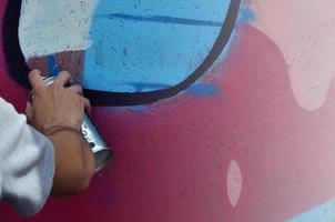 A hand with a spray can that draws a new graffiti on the wall. Photo of the process of drawing a graffiti on a wooden wall close-up. The concept of street art and illegal vandalism