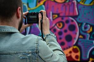 un joven grafitero fotografía su cuadro completo en la pared. el chico usa tecnología moderna para capturar un colorido dibujo de graffiti abstracto. centrarse en el dispositivo de fotografía foto