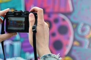 un joven grafitero fotografía su cuadro completo en la pared. el chico usa tecnología moderna para capturar un colorido dibujo de graffiti abstracto. centrarse en el dispositivo de fotografía foto