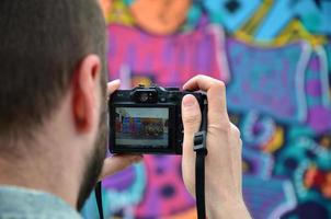 un joven grafitero fotografía su cuadro completo en la pared. el chico usa tecnología moderna para capturar un colorido dibujo de graffiti abstracto. centrarse en el dispositivo de fotografía foto