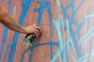 A hand with a spray can that draws a new graffiti on the wall. Photo of the process of drawing a graffiti on a wooden wall close-up. The concept of street art and illegal vandalism