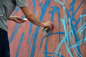 una mano con un bote de spray que dibuja un nuevo grafiti en la pared. foto del proceso de dibujar un graffiti en un primer plano de la pared de madera. el concepto de arte callejero y vandalismo ilegal