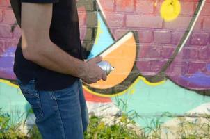 Young graffiti artist with shows your spraycan as a penis from denims fly zipper against colorful pink graffiti painting on brick wall photo