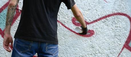 A young hooligan paints graffiti on a concrete wall. Illegal vandalism concept. Street art photo