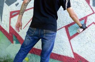 A young hooligan paints graffiti on a concrete wall. Illegal vandalism concept. Street art photo