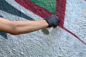 A hand in black gloves paints graffiti on a concrete wall. Illegal vandalism concept. Street art photo
