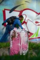 A few used paint cans against the background of the space with the wall on which the young guy draws a large graffiti drawing. Modern art of drawing walls in graffiti photo