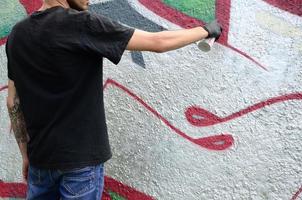 A young hooligan paints graffiti on a concrete wall. Illegal vandalism concept. Street art photo