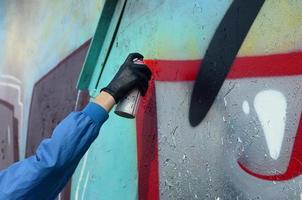 una mano con un bote de spray que dibuja un nuevo grafiti en la pared. foto del proceso de dibujo de un graffiti en una pared de metal. el concepto de arte callejero y vandalismo ilegal