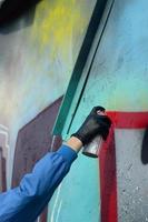 A hand with a spray can that draws a new graffiti on the wall. Photo of the process of drawing a graffiti on a metal wall. The concept of street art and illegal vandalism