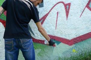 A young hooligan paints graffiti on a concrete wall. Illegal vandalism concept. Street art photo