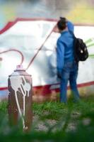 A few used paint cans against the background of the space with the wall on which the young guy draws a large graffiti drawing. Modern art of drawing walls in graffiti photo