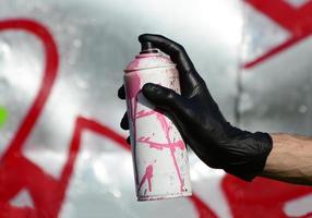 A hand with a spray can that draws a new graffiti on the wall. Photo of the process of drawing a graffiti on a metal wall. The concept of street art and illegal vandalism