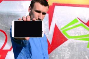 The graffiti artist demonstrates a smartphone with an empty black screen against the background of a colorful painted wall. Street art concept photo