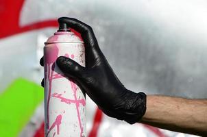 A hand with a spray can that draws a new graffiti on the wall. Photo of the process of drawing a graffiti on a metal wall. The concept of street art and illegal vandalism
