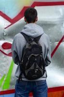 A young graffiti artist with a black bag looks at the wall with his graffiti on a wall. Street art concept photo