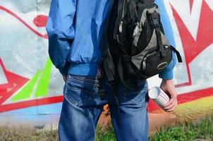 un joven artista de graffiti con una bolsa negra mira la pared con su graffiti en una pared. concepto de arte callejero foto