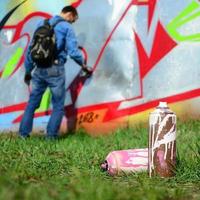 A few used paint cans against the background of the space with the wall on which the young guy draws a large graffiti drawing. Modern art of drawing walls in graffiti photo