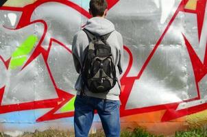 A young graffiti artist with a black bag looks at the wall with his graffiti on a wall. Street art concept photo