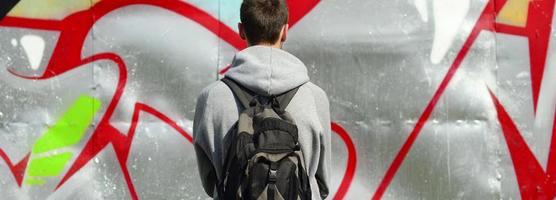 A young graffiti artist with a black bag looks at the wall with his graffiti on a wall. Street art concept photo