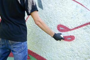 A young hooligan paints graffiti on a concrete wall. Illegal vandalism concept. Street art photo