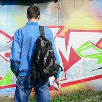 A young graffiti artist with a black bag looks at the wall with his graffiti on a wall. Street art concept photo