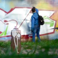 A few used paint cans against the background of the space with the wall on which the young guy draws a large graffiti drawing. Modern art of drawing walls in graffiti photo