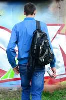 A young graffiti artist with a black bag looks at the wall with his graffiti on a wall. Street art concept photo