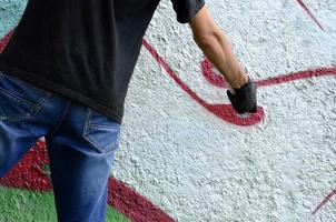 A young hooligan paints graffiti on a concrete wall. Illegal vandalism concept. Street art photo